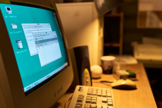 Old CRT computer monitor displaying classic graphical user interface with open text editor windows, keyboard and mouse on wooden desk in retro office workspace