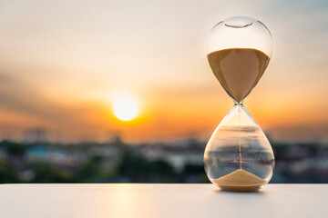 Hourglass on table at sunset with blurred city background symbolizing passing time, limited...