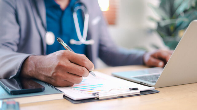Close-up of professional writing financial report on clipboard at office desk with laptop and smartphone. Concept of analysis, documentation, planning, and consulting work.