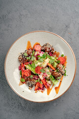 Sesame-coated glazed beef with fresh salad greens, halved cherry tomatoes, shredded carrots and soy-based dressing in white bowl. Exotic teriyaki beef salad, colorful healthy lunch or dinner