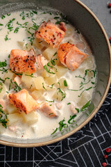 Creamy potato soup topped with seared salmon pieces and chopped herbs in ceramic bowl. Rich Nordic salmon chowder, wholesome seafood meal, top view, close up