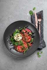 Fresh tomato carpaccio with creamy burrata, pesto drizzle, fresh basil leaves and balsamic glaze on black plate. Elegant Italian appetizer, gourmet salad-style dish, restaurant presentation, top view