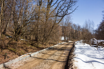 Fototapeta premium New urban path taking shape: freshly installed curbs line a gravel road, blending spring construction with thawing nature and bare trees