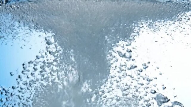 A dynamic close-up shows water vigorously swirling and bubbling A central stream of turbulent water descends amidst numerous scattered air bubbles set against a light blue background