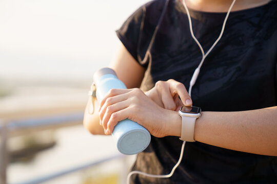 Asian woman checking smartwatch while walking outdoors. Virtual fitness assistant technology.