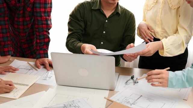 Smart architect and safety engineer discussion about building plan on table with architectural document, measurement tools and wooden block scatter around at modern office. Closeup. Delineation.