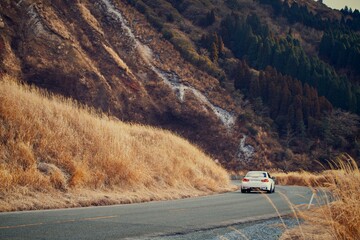 Car driving along a winding mountain road through dry grassland scenery