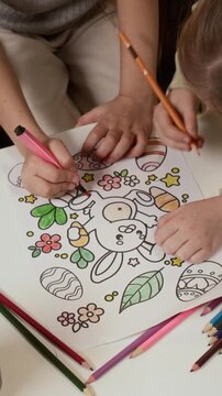 Vertical high angle cropped shot of hands of unrecognizable creative children coloring Easter rabbit using pencils and markers