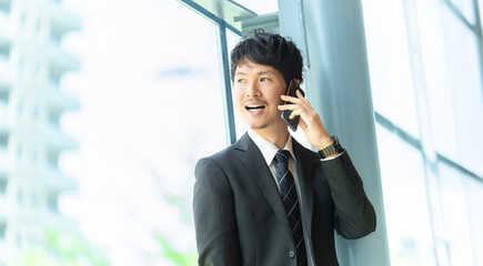 窓際で電話対応をするビジネスマン, Businessman Talking on Smartphone by Office Window