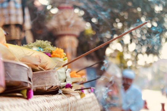 Balinese canang sari offering with burning incense in front of a pura temple, Kuta, Bali, Indonesia. Close-up side angle, shallow focus and soft smoke create a peaceful, spiritual mood. Ideal for reli