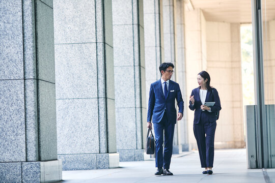 会話をしながら屋外を歩くビジネスマンとビジネスウーマン