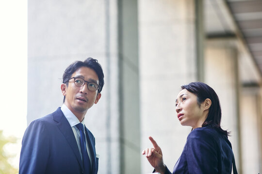 会話をしながら屋外を歩くビジネスマンとビジネスウーマン