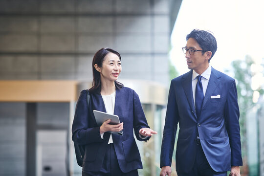 会話をしながら屋外を歩くビジネスマンとビジネスウーマン