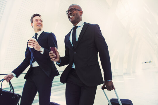 Diverse smiling businessmen rushing down an airport hall for a flight. They are traveling on a business engagement, with a cabin-sized suitcase and passport in hand.