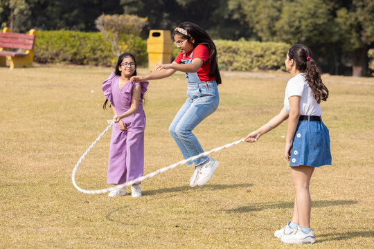 Three indian kid friends play skipping rope together in summer park, Children having fun playing outdoor activity. Childhood.
