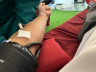 Medical professional wearing blue gloves inserting needle into patient. Person lying on medical chair with intravenous drip attached to their arm for blood transfusion or donation.