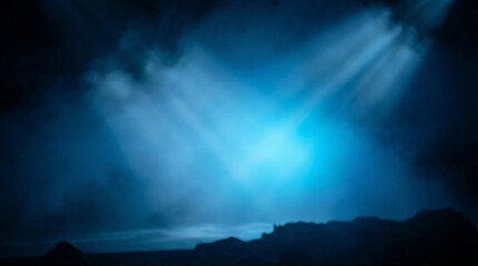 Obraz premium Blurred blue light beams cut through atmospheric fog over dark, rugged terrain, evoking a sense of mystery and exploration.