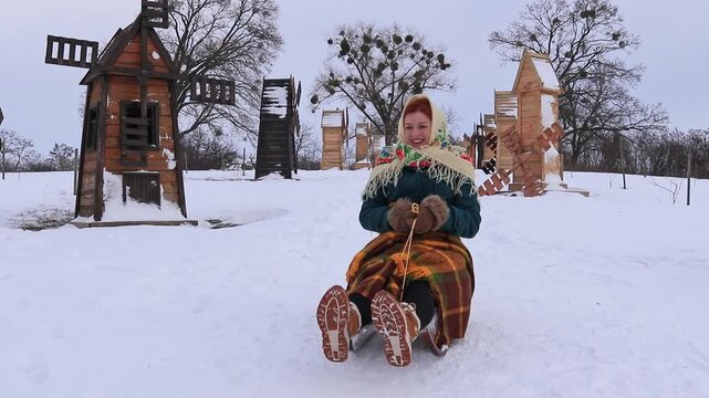 Beautiful girl sledding with a smile on her face. Joyful atmosphere, snow, active recreation, traditional clothing, beauty of nature and winter entertainment.