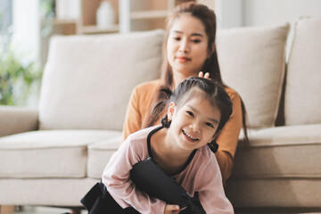 Obraz premium A cheerful Asian mother helps her young daughter do homework and color a book at home, while the father works on a laptop in the background. A cozy, bright, and modern family lifestyle.