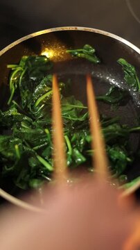 Woman frying fresh spinach in kitchen