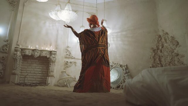 Beautiful lady dancing on sand in studio with crystal chandeliers, luxury Africa . Female shaman performing ritual for asking rain in desert, richness and wealth of arabian palace, african princess
