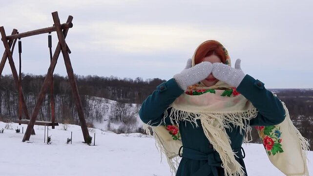 Beautiful girl with red hair closes her eyes with winter mittens. Atmospheric winter landscape, calm nature and cold day. Portrait of a beautiful girl