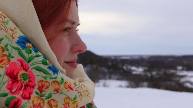 Close-up of a young Ukrainian woman in a traditional floral scarf against a winter rural landscape. Authentic culture and folk traditions.