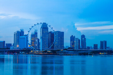 A modern building with a giant Ferris wheel by the sea, at twilight, overlooking the Singapore skyline.
