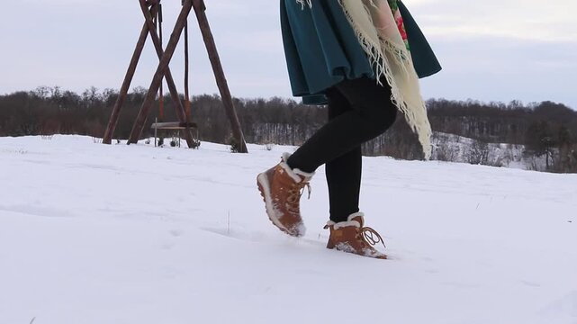 Woman's legs in winter boots slowly walk through the snow against the backdrop of a rural landscape. Atmosphere of calm, winter walk, minimalism and lifestyle.