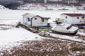 Snowy riverside houseboats and small boats docked near a frozen winter river