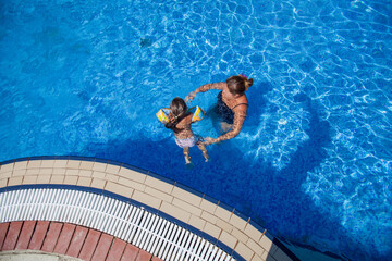 Overhead view of a mother and children swimming in a large blue resort pool.