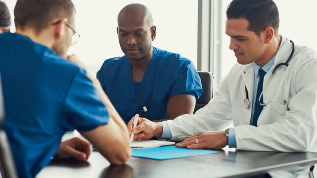 Young focused African American male doctor in medical staff meeting, together with colleagues they take notes