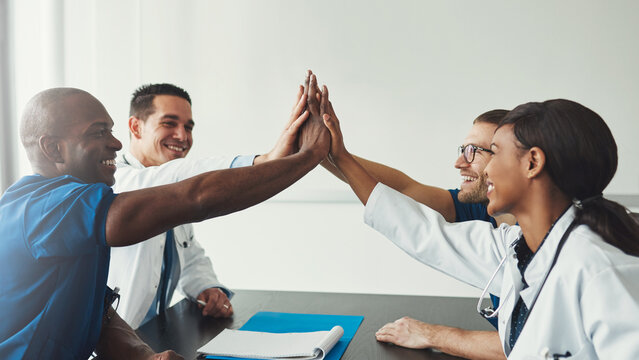 Young diverse medical specialists high five each other to celebrate a success at the hospital.