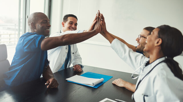 Young multiracial medical specialists high five each other to celebrate a success at the hospital.