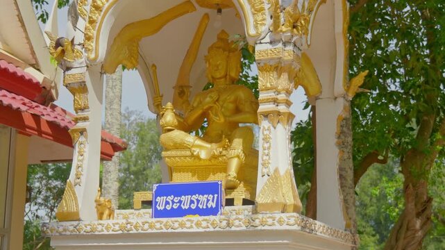 Close-up of a golden Phra Phrom (Brahma) statue with four faces inside an ornate white and gold shrine. Captured at Wat Nai Harn temple in Phuket, Thailand. 4K cinematic travel footage.