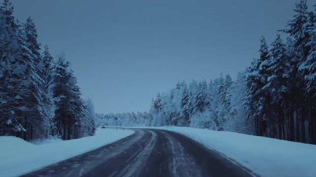 Car is driving on a frozen road in ice. Driver drives a car on a snowy highway in winter. Polar night in Arctic pine forest. Cold weather. Blizzard in winter journey, outdoor. Snowstorm in road trip.