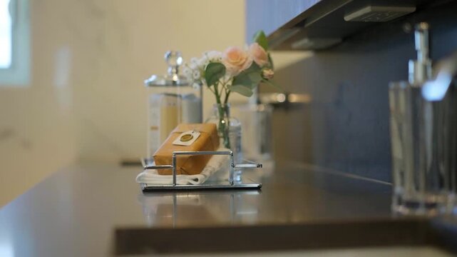 Elegant bathroom countertop featuring a soap bar, glass dispenser, and soft floral decor, showcasing modern luxury and clean interior styling.