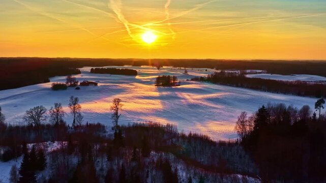 Golden sun illuminating a tranquil snowy winter landscape with trees and distant hills under a vibrant sky