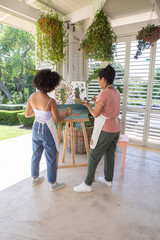 Obraz premium Mother and daughter painting canvas on covered home patio using wooden easel and paint palette