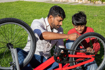 Indian father with son repairing red bicycle frame upside down on backyard lawn using spanner © wavebreak3