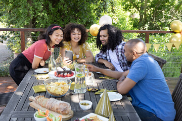Diverse friends checking smartphone at patio table while sipping lemon water, tasting cupcakes © wavebreak3