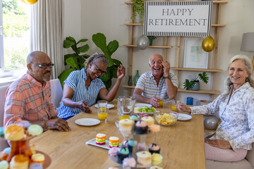 Diverse senior friends celebrating retirement in dining room at table with banner, balloons