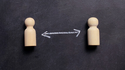 Two wooden peg dolls separated by a chalk arrow for social distancing and human relationship concept