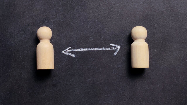 Two wooden peg dolls separated by a chalk arrow for social distancing and human relationship concept