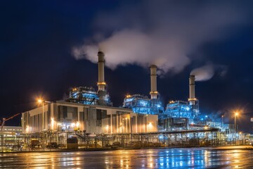 Fototapeta premium Industrial facility exterior under night sky, illuminated infrastructure and smokestacks