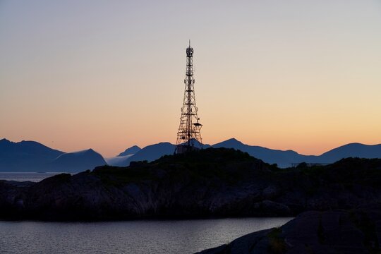 A communications mast is silouetted against a pink and orange sky lit by the setting sun, in the fishing village of Henningsvaer, Norway.