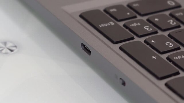 A human hand pulls out or inserts a USB Type-C cable into a laptop, Hand inserting a white charging plug into a grey notebook.