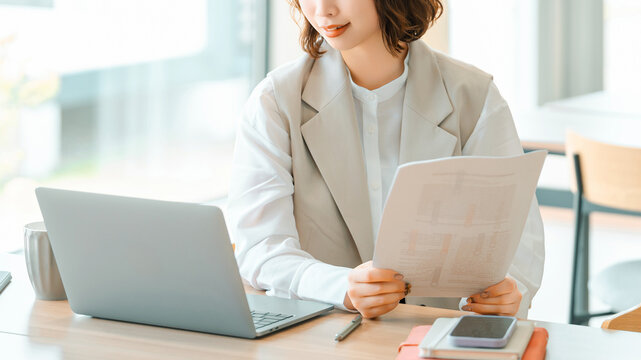 ノートパソコンで資料を確認するビジネスウーマン, Businesswoman Checking Documents on Laptop at Desk