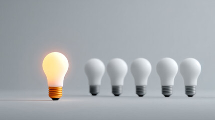 Unique light bulb shines bright. One bright light bulb is in front of four off bulbs on a gray background, showing contrast in a simple arrangement.