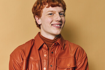 Obraz premium Young man with red hair wearing orange shirt and turtleneck smiling confident against beige background, portrait with casual style and positive expression.